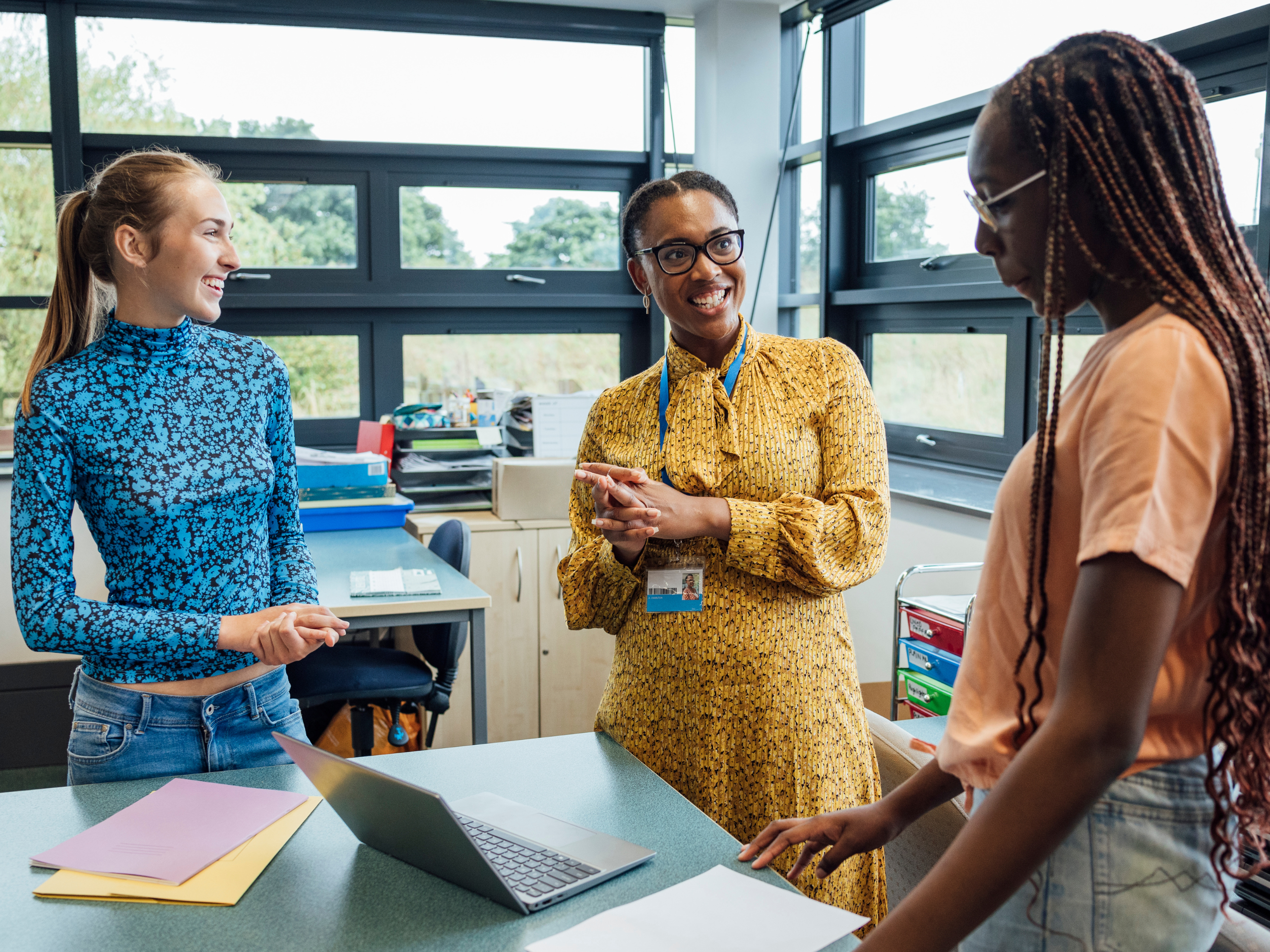 A diverse group of three women engaged in a positive and collaborative discussion in a well-lit classroom